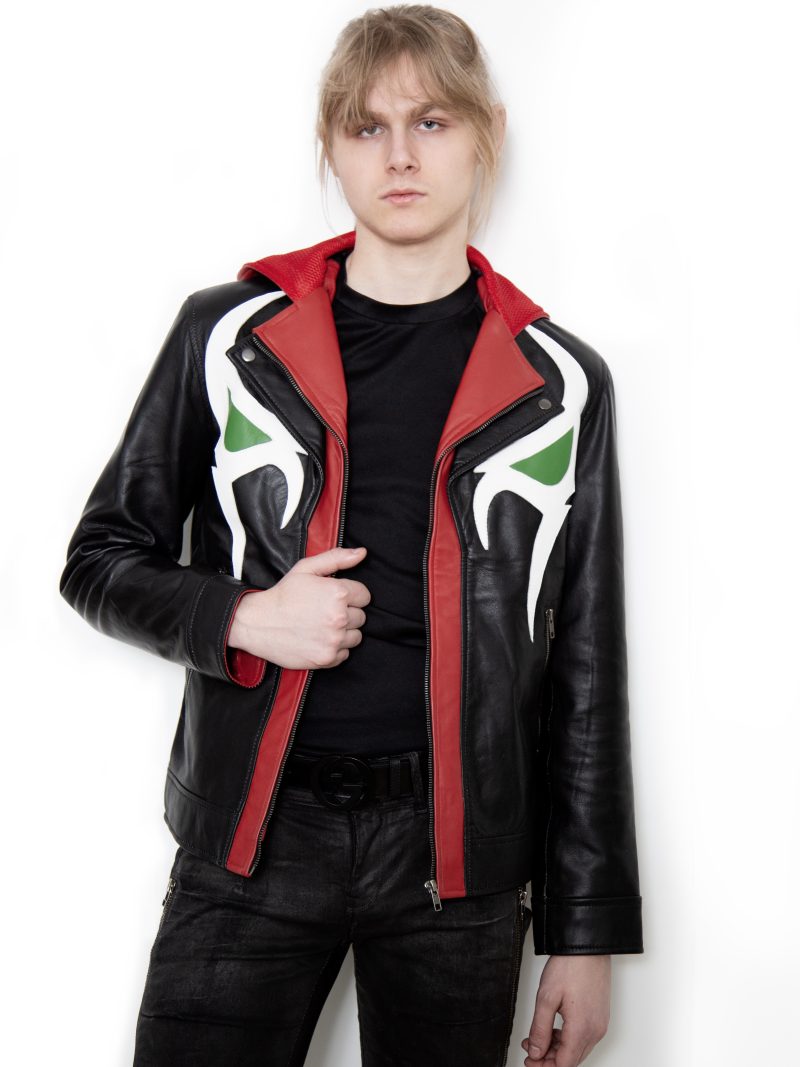 (Front): Photo of a model wearing a black leather jacket. The jacket is a motorcycle cut with a red hood and a red leather lining that is visible inside the cuffs and the folded down collar. There is also a strip of red leather either side of the front zipper. Where breast pockets typically would be on a jacket, there are [handpainted/patched] green eyes surrounded by white details. The collar has metal pop buttons to hold it in place. (Back): Photo of the same black leather jacket with a red hood. The jacket is a motorcycle cut. The inside of the hood has a mesh lining.