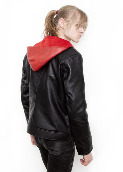 (Front): Photo of a model wearing a black leather jacket. The jacket is a motorcycle cut with a red hood and a red leather lining that is visible inside the cuffs and the folded down collar. There is also a strip of red leather either side of the front zipper. Where breast pockets typically would be on a jacket, there are [handpainted/patched] green eyes surrounded by white details. The collar has metal pop buttons to hold it in place. (Back): Photo of the same black leather jacket with a red hood. The jacket is a motorcycle cut. The inside of the hood has a mesh lining.